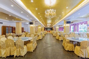 A banquet hall with round tables and chairs, a stage, and a chandelier.