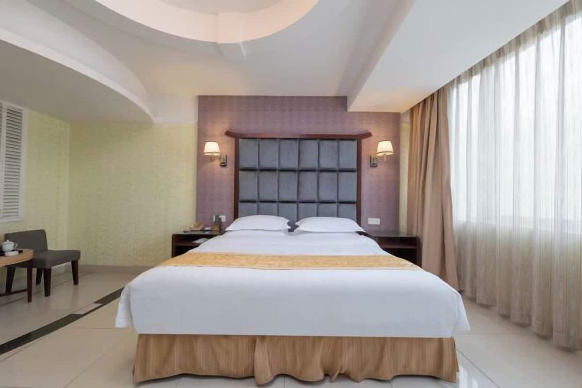 Habitació d'hotel amb un llit gran, una taula de treball, una cadira i una finestra amb cortines.