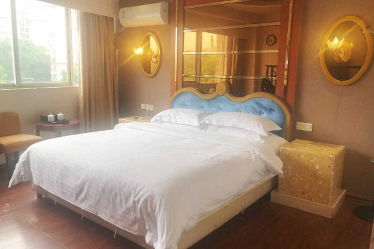 A hotel room with a large bed, a bedside table, a mirror, and a window.
