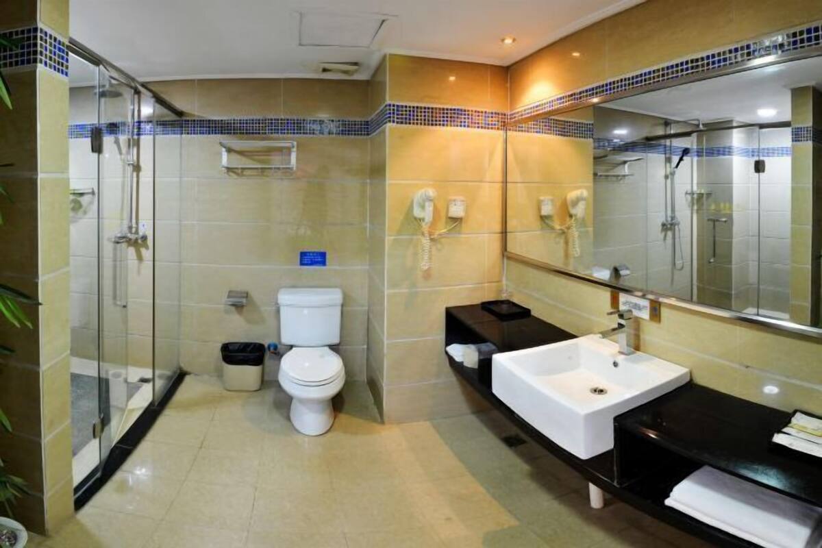 Un bany modern amb una dutxa de vidre, un vàter blanc, un lavabo negre i un mirall gran.