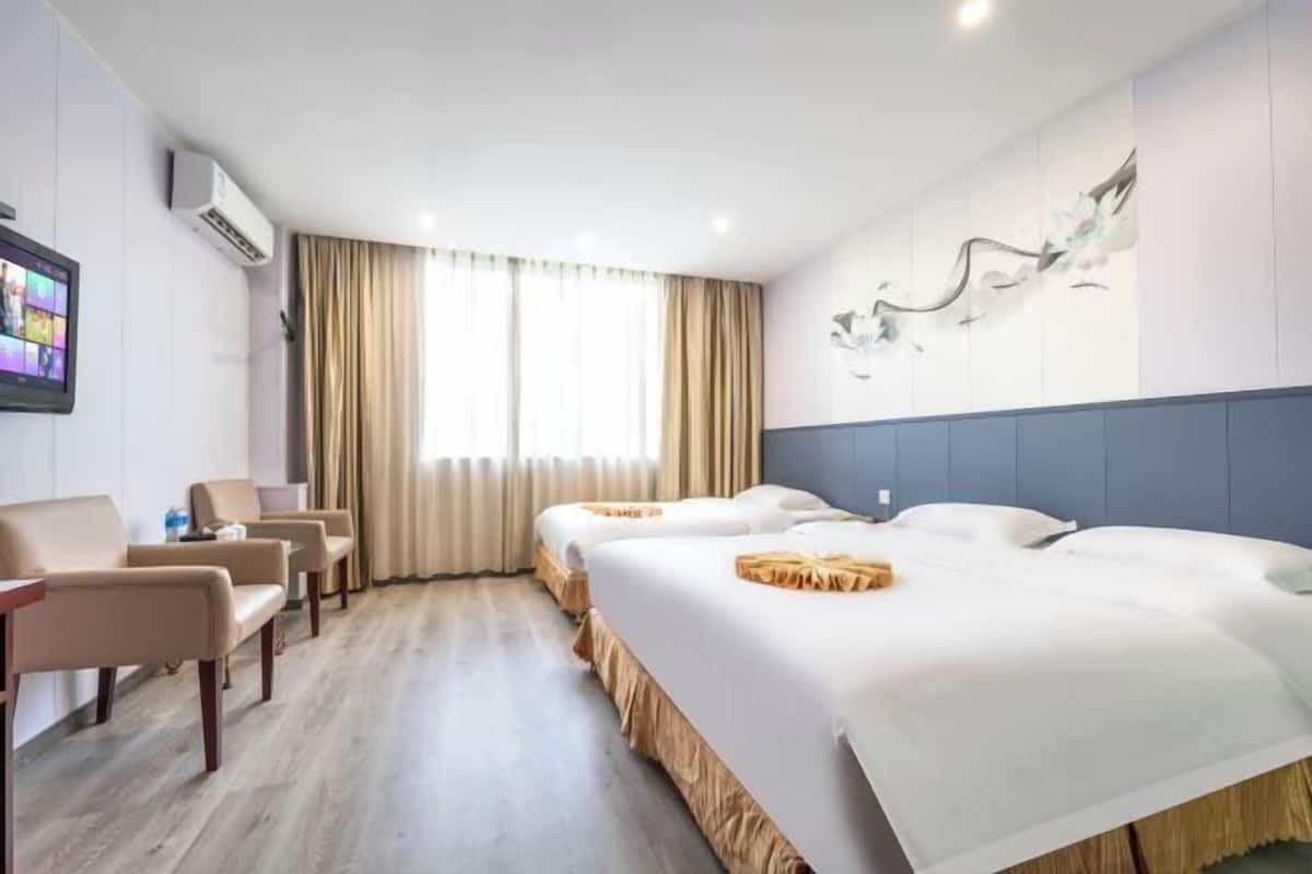 Habitació d'hotel amb dos llits, zona de seients, televisió i aire condicionat fixat a la paret.