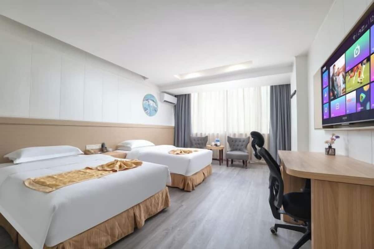 Habitació d'hotel amb dos llits, escriptori, cadira, televisió i finestra amb cortines.