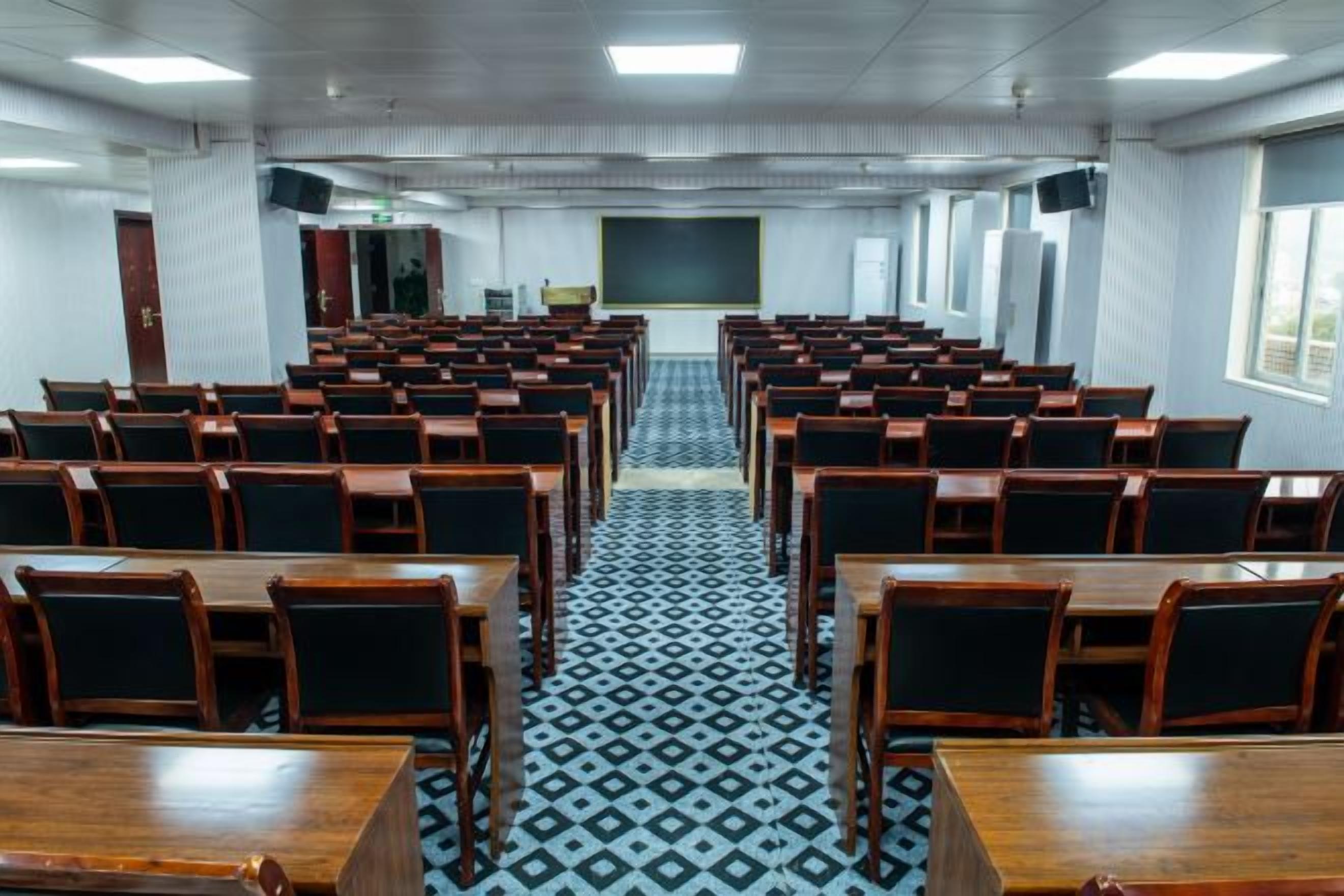 A conference room with rows of tables and chairs, a patterned floor, and a presentation screen at the front.