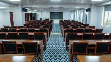 Un salón de conferencias con filas de mesas y sillas, un piso estampado y una pantalla para presentaciones al frente.