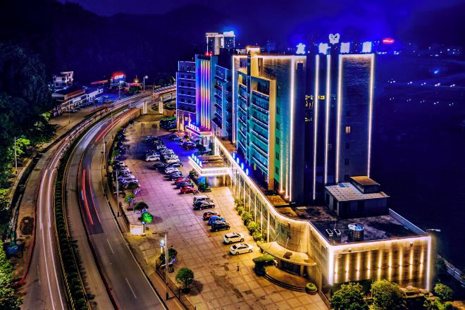 A multi-story hotel with a parking lot, a road curving around it, and a mountainous backdrop.
