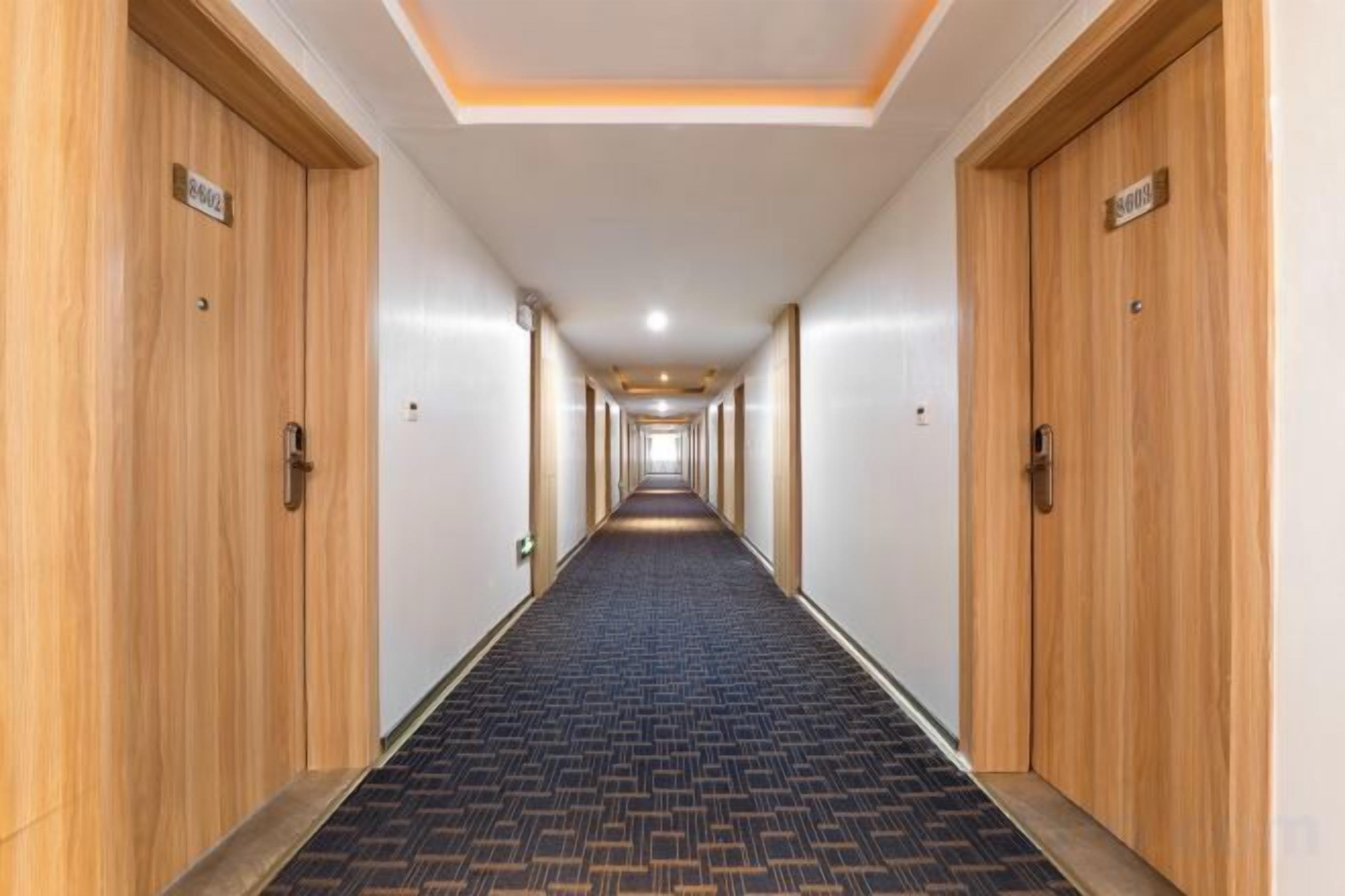 A hotel corridor with wooden doors, a patterned carpet, and a ceiling with recessed lighting.