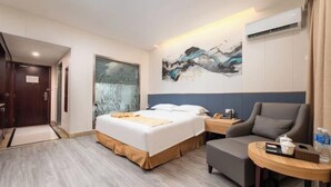 Quarto de hotel com cama, uma cadeira, uma mesinha e um quadro na parede.
