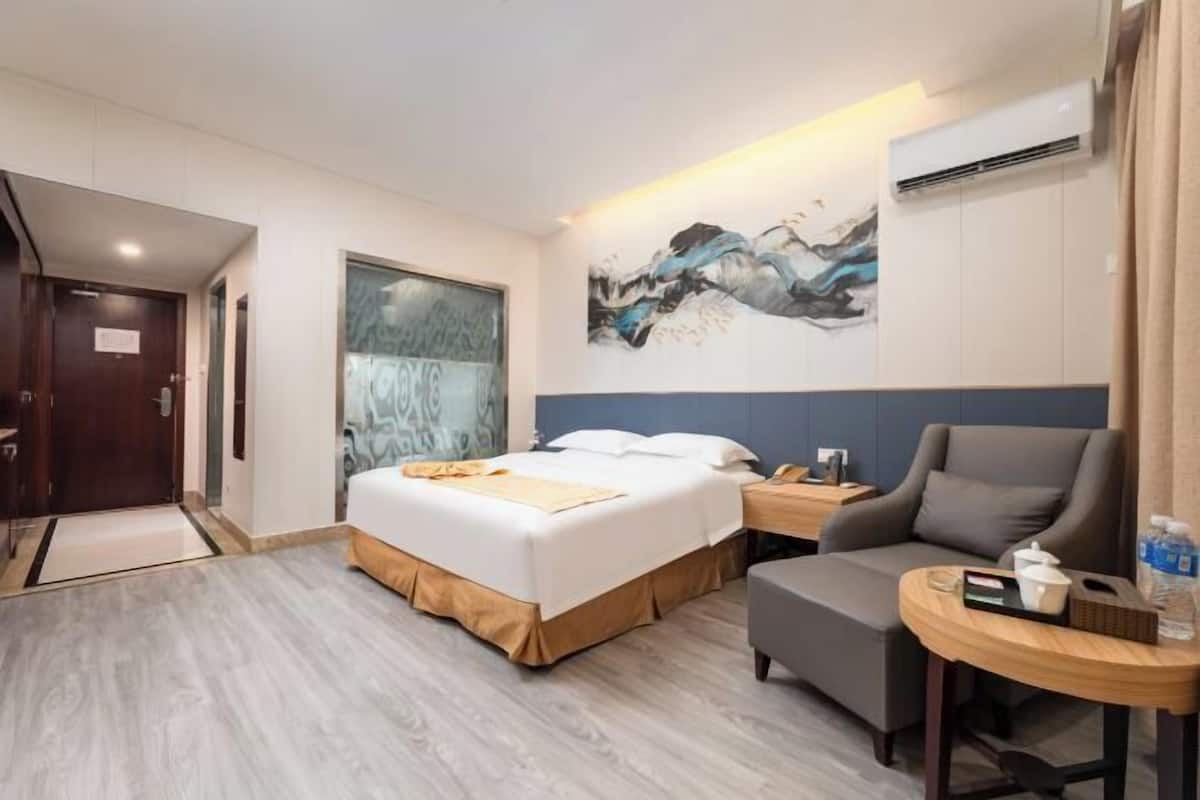 Habitació d'hotel amb un llit, una cadira, una taula petita i un quadre a la paret.