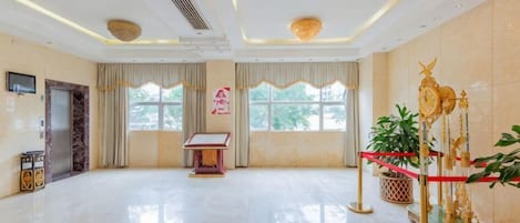 A spacious hotel lobby with a marble floor, a reception desk, and a large window offering a view of the outdoors.