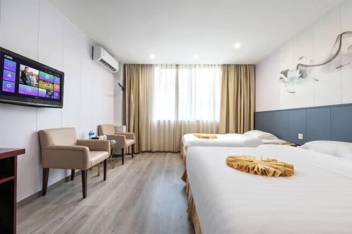 A hotel room with a bed, a desk, a chair, a TV mounted on the wall, and a window with curtains.