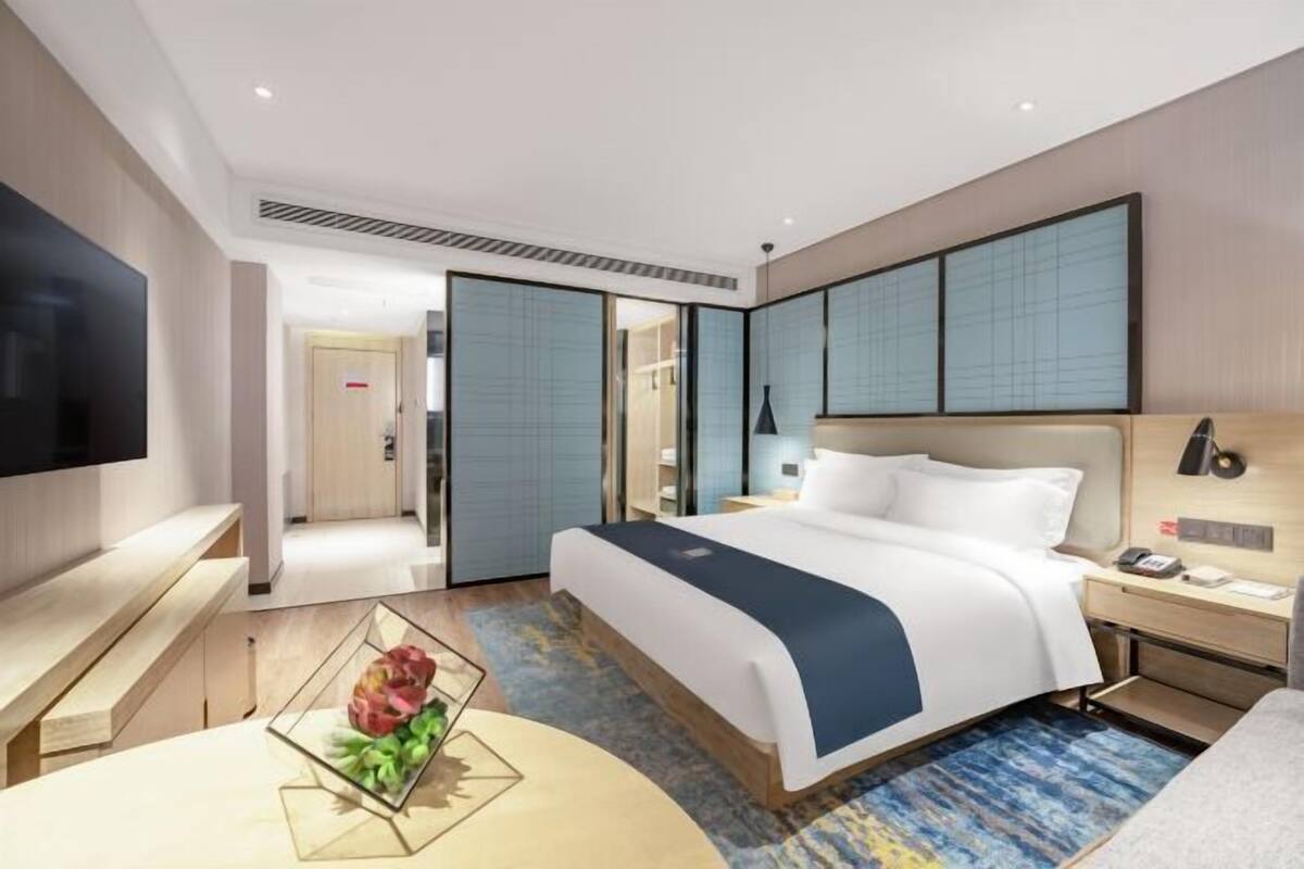 A modern hotel room with a large bed, bedside tables, a flat-screen TV, and a view of the hallway.
