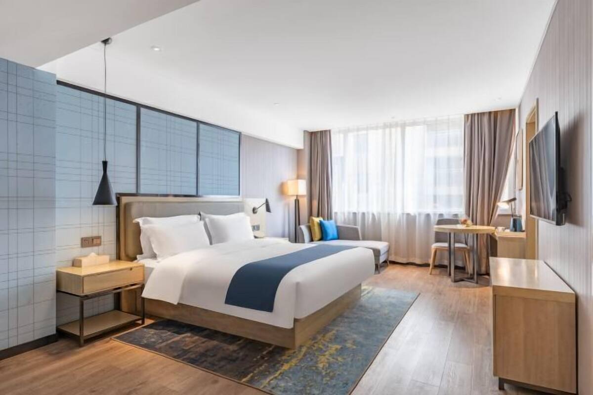 A modern hotel room with a large bed, bedside tables, a desk, and a TV.