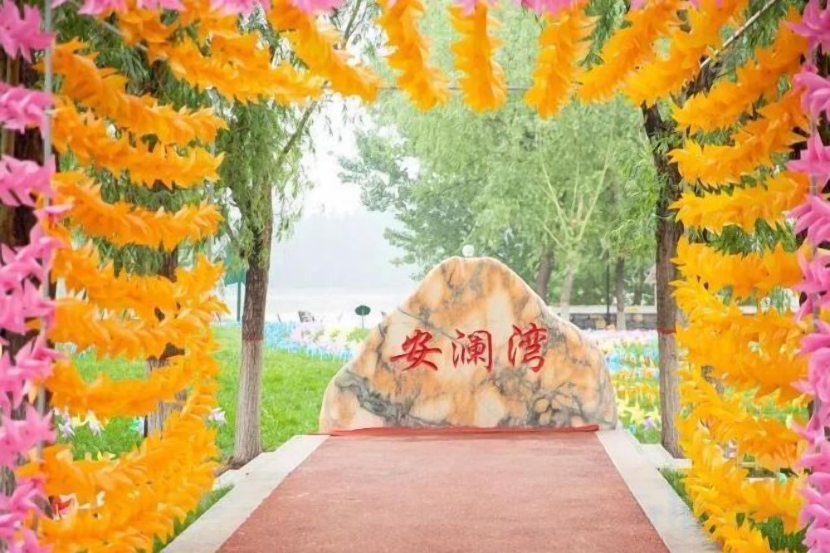 Ein Weg führt zu einem Felsen mit chinesischen Schriftzeichen, umgeben von gelben und rosa Blumen.