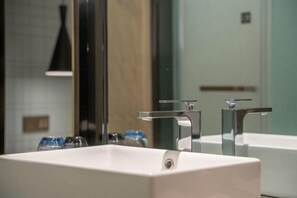 A bathroom with a white sink, two chrome faucets, and a mirror.