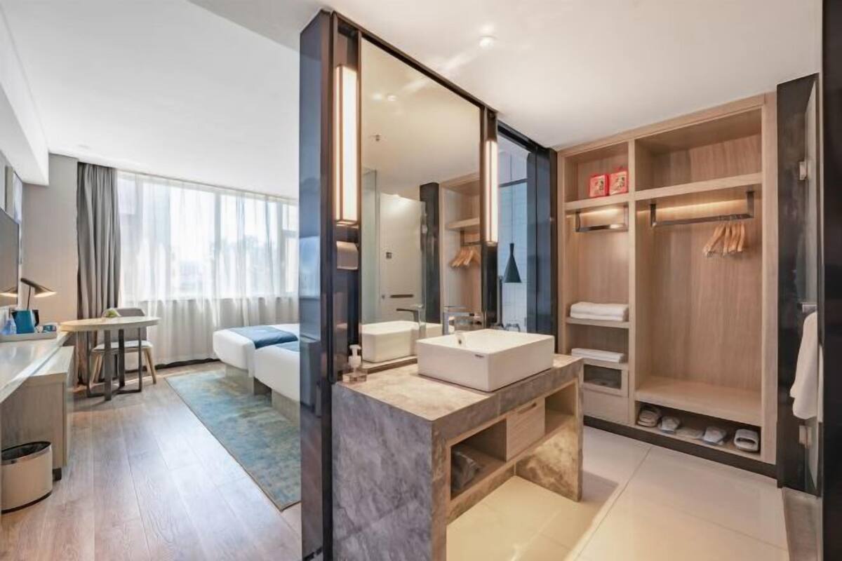 A modern hotel bathroom with a large mirror, two sinks, a vanity, and a walk-in closet.