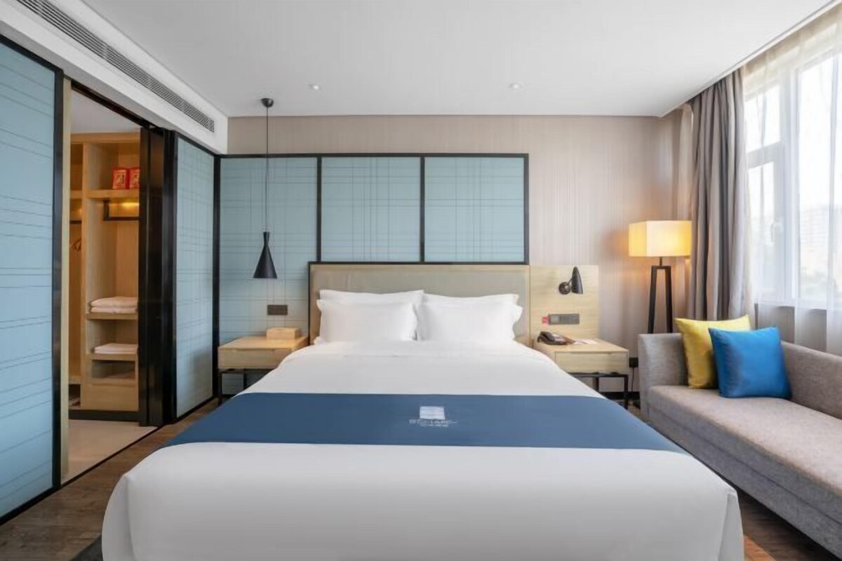 A hotel room with a large bed, a sofa, a desk, a lamp, and a sliding door leading to a closet.
