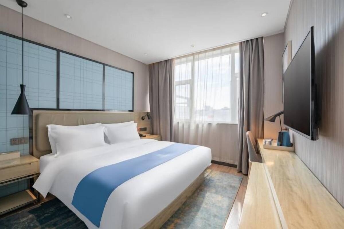 A hotel room with a large bed, a flat-screen TV, a desk, and a window with curtains.