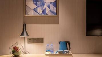 A hotel room with a wooden table, a geometric vase, a lamp, a coffee maker, and a flat-screen TV.