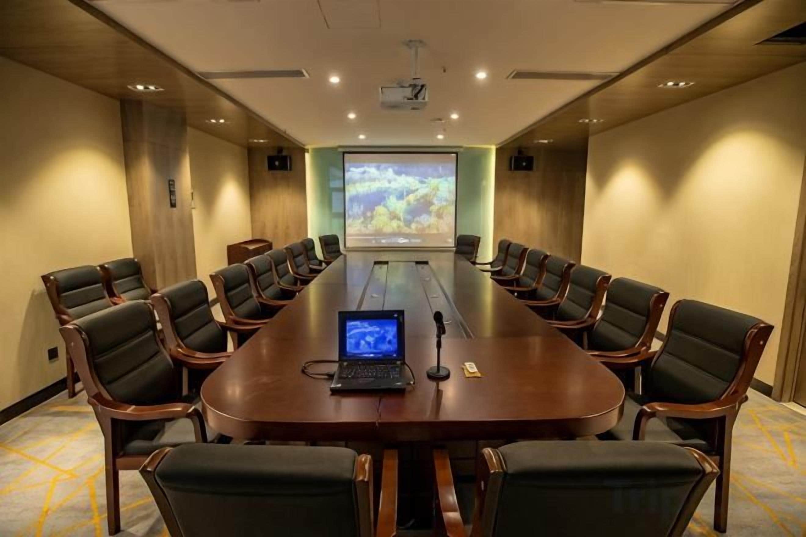 A conference room with a long table, chairs, a laptop, a projector screen, and a presentation.