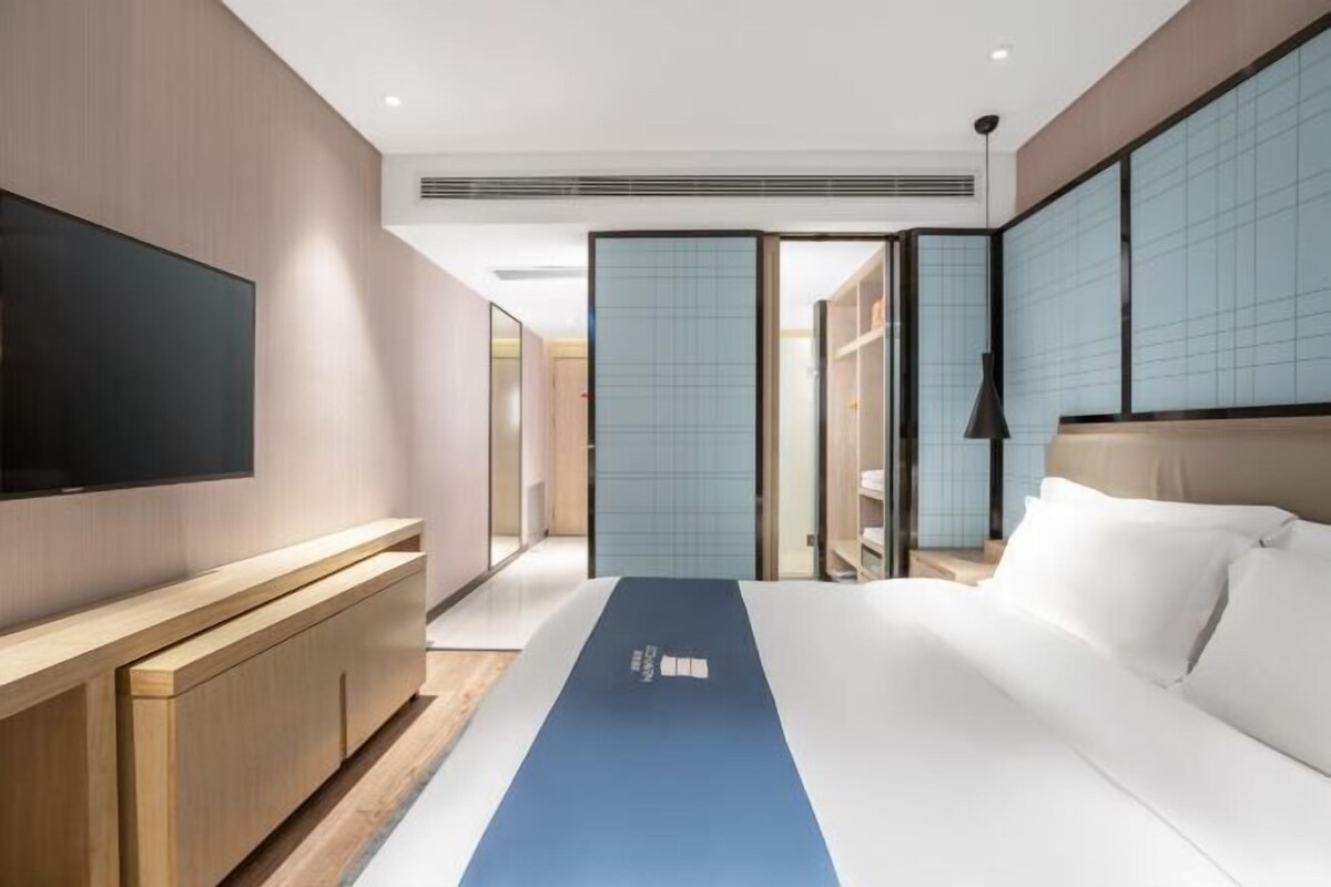 A modern hotel room with a large bed, a flat-screen TV, a wooden console, and a sliding door leading to a bathroom.