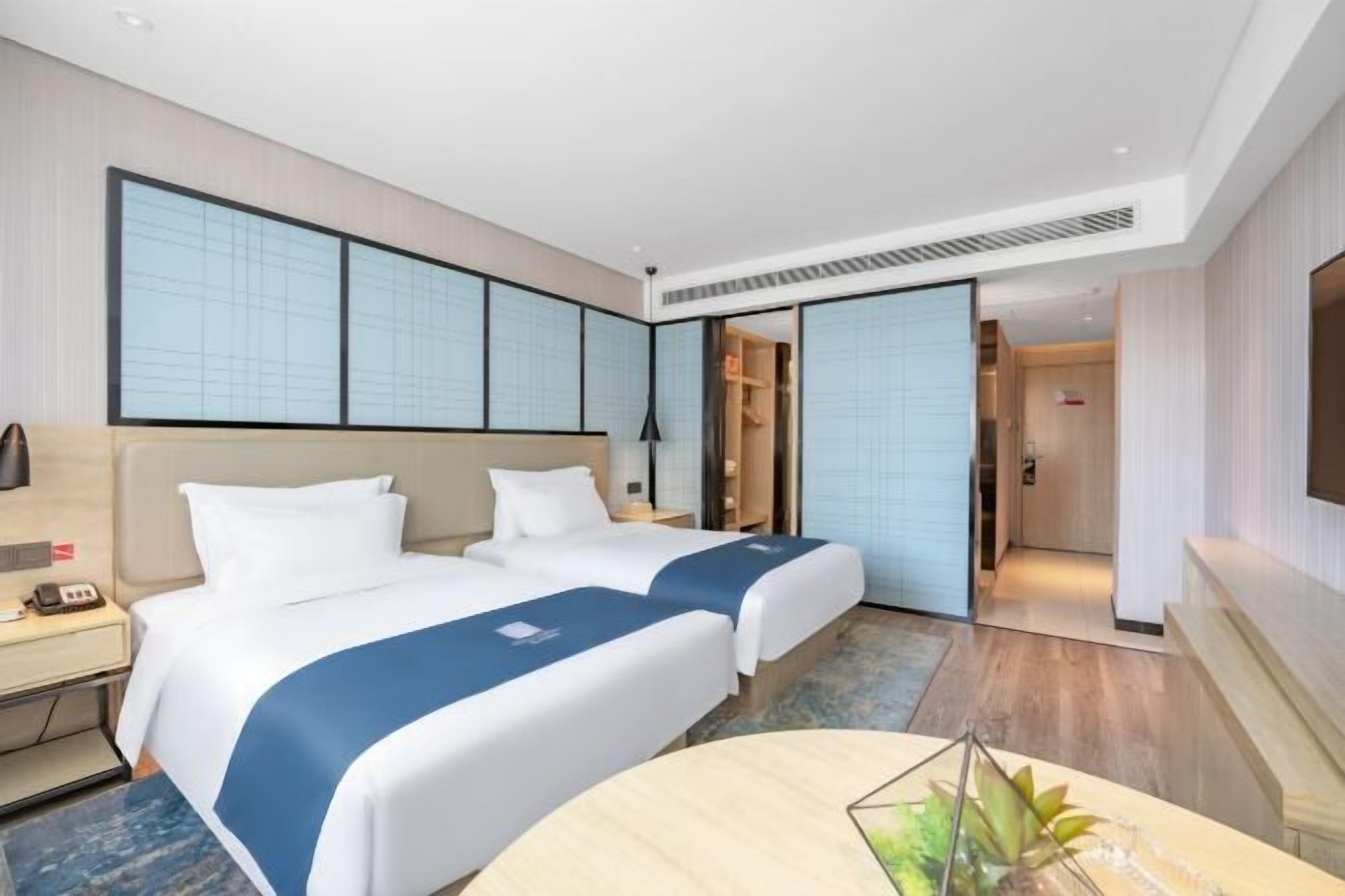 A hotel room with two beds, a desk, a chair, and a TV.