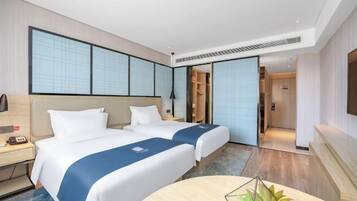 A hotel room with two beds, a desk, a chair, and a TV.