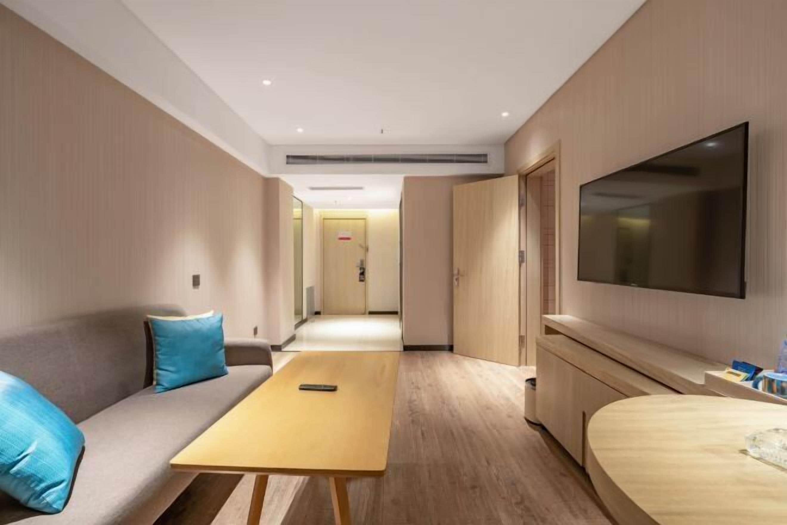 A hotel room with a sofa, a small table, a TV, and a bed.