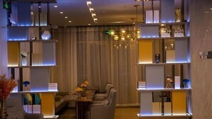 A modern interior with a dining area, sofas, and shelves with decorative items. - Echarm Hotel (Gaoqing Zhongcheng International) (Gaoqing)