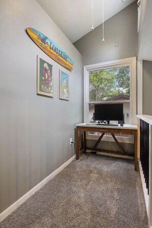 A hallway with a grey carpet, a wooden desk with a computer, a TV, and framed pictures on the wall. - The Lake Front Oasis in Eldon•Near Bagnell Dam (Eldon)