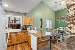 A kitchen with wooden cabinets, a granite countertop, a dishwasher, and a dining area with white chairs. - The Lake Front Oasis in Eldon•Near Bagnell Dam (Eldon)