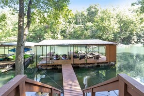 A floating dock with a covered seating area, boats, and a wooden walkway leading to it. - The Lake Front Oasis in Eldon•Near Bagnell Dam (Eldon)