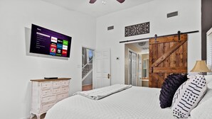 A bedroom with a bed, a dresser, a TV mounted on the wall displaying streaming services, and a barn-style door. - Hot Tub/Shuffleboard/Pool Table near Guadalupe Riv. & Lake (New Braunfels)