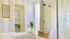 Habitación de hotel con cama, espejo, baño visible a través de una puerta abierta y una planta.
