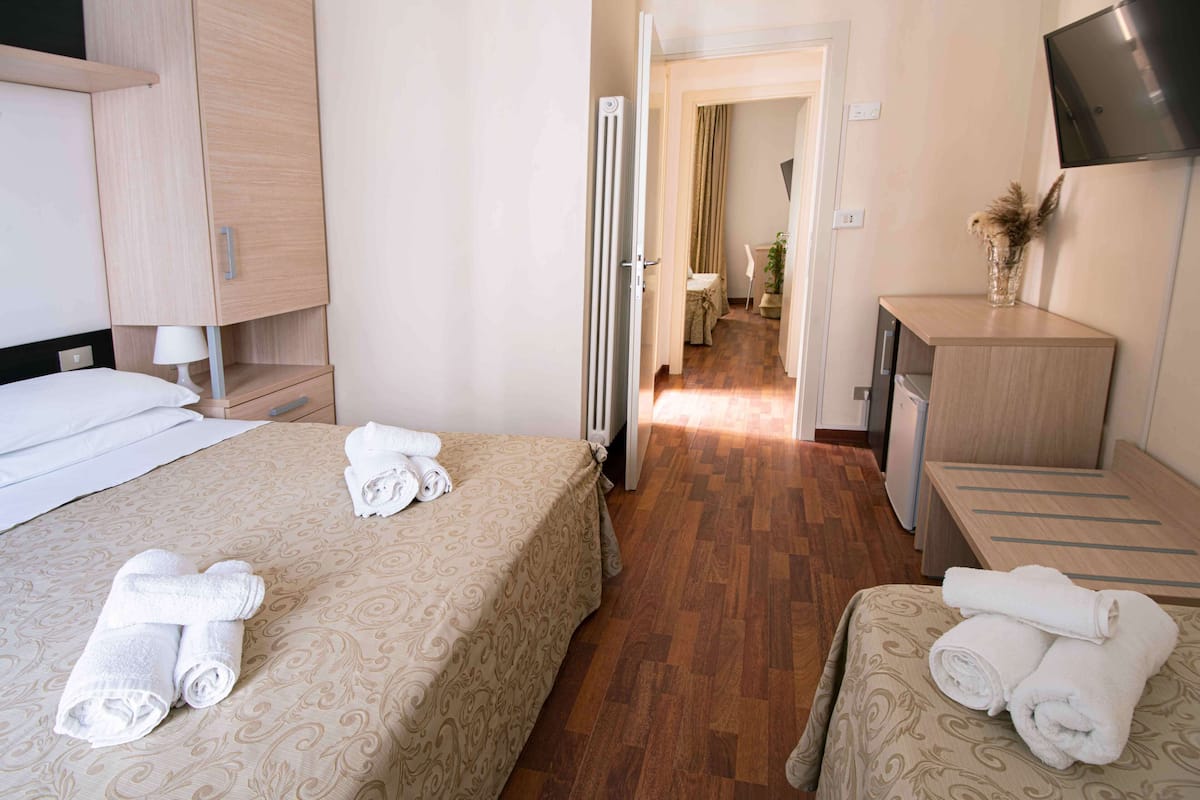 Une chambre d’hôtel avec deux lits, un bureau, un radiateur et un téléviseur fixé au mur.