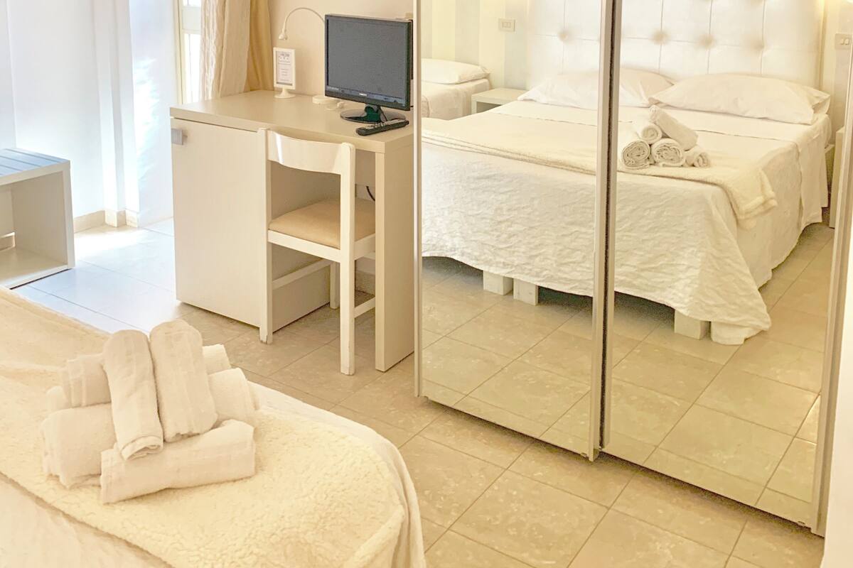 Une chambre d’hôtel comprenant un lit, un bureau avec un ordinateur, un miroir et une salle de bain avec un rideau de douche.