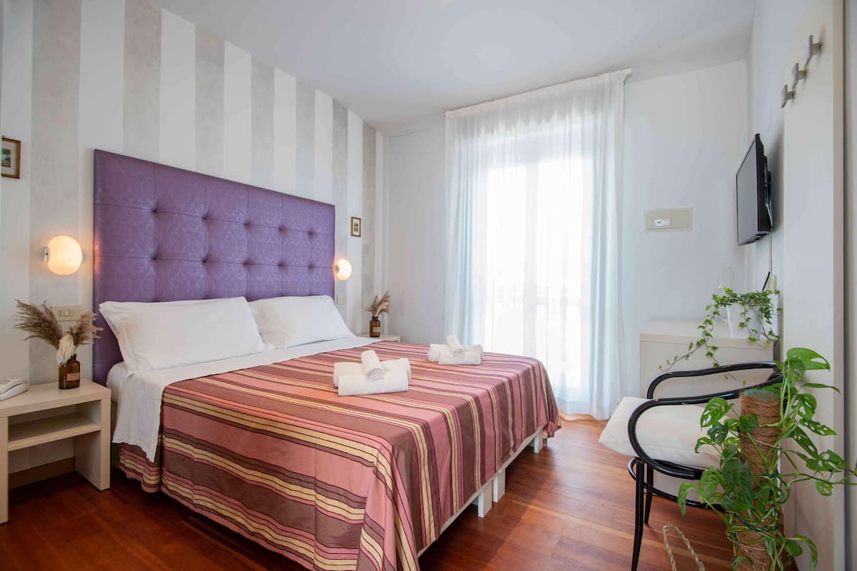 Une chambre à coucher bien rangée, avec un lit, des tables de chevet, une chaise, un téléviseur et une fenêtre avec des rideaux.