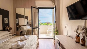 Habitación de hotel con cama, escritorio, televisión y balcón con vista al océano.