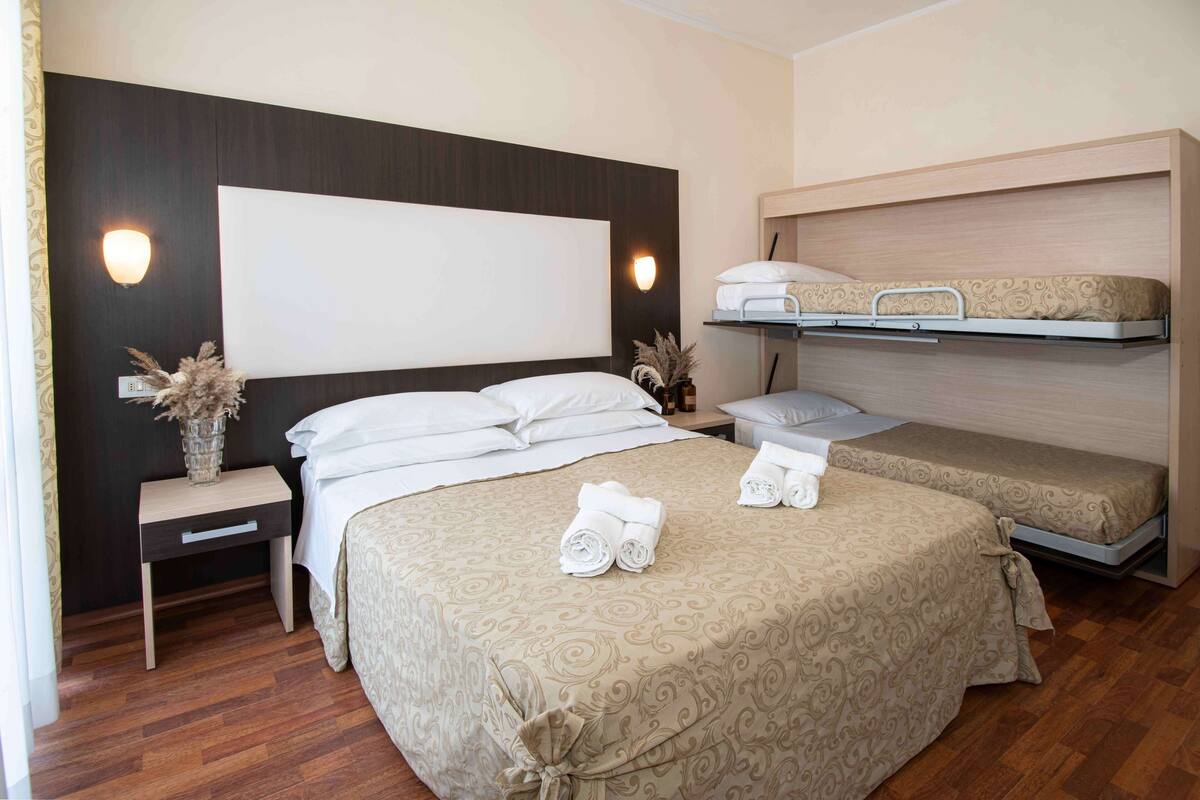 Une chambre d’hôtel avec un grand lit, un lit plus petit, une table de chevet et une étagère fixée au mur.