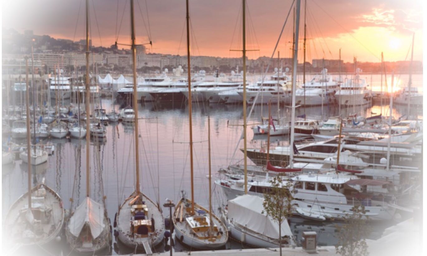 Un puerto deportivo con varias embarcaciones amarradas, un paisaje urbano al fondo y un atardecer.