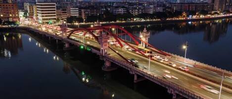 A nighttime cityscape with a prominent red bridge over a river, surrounded by buildings and illuminated streets.