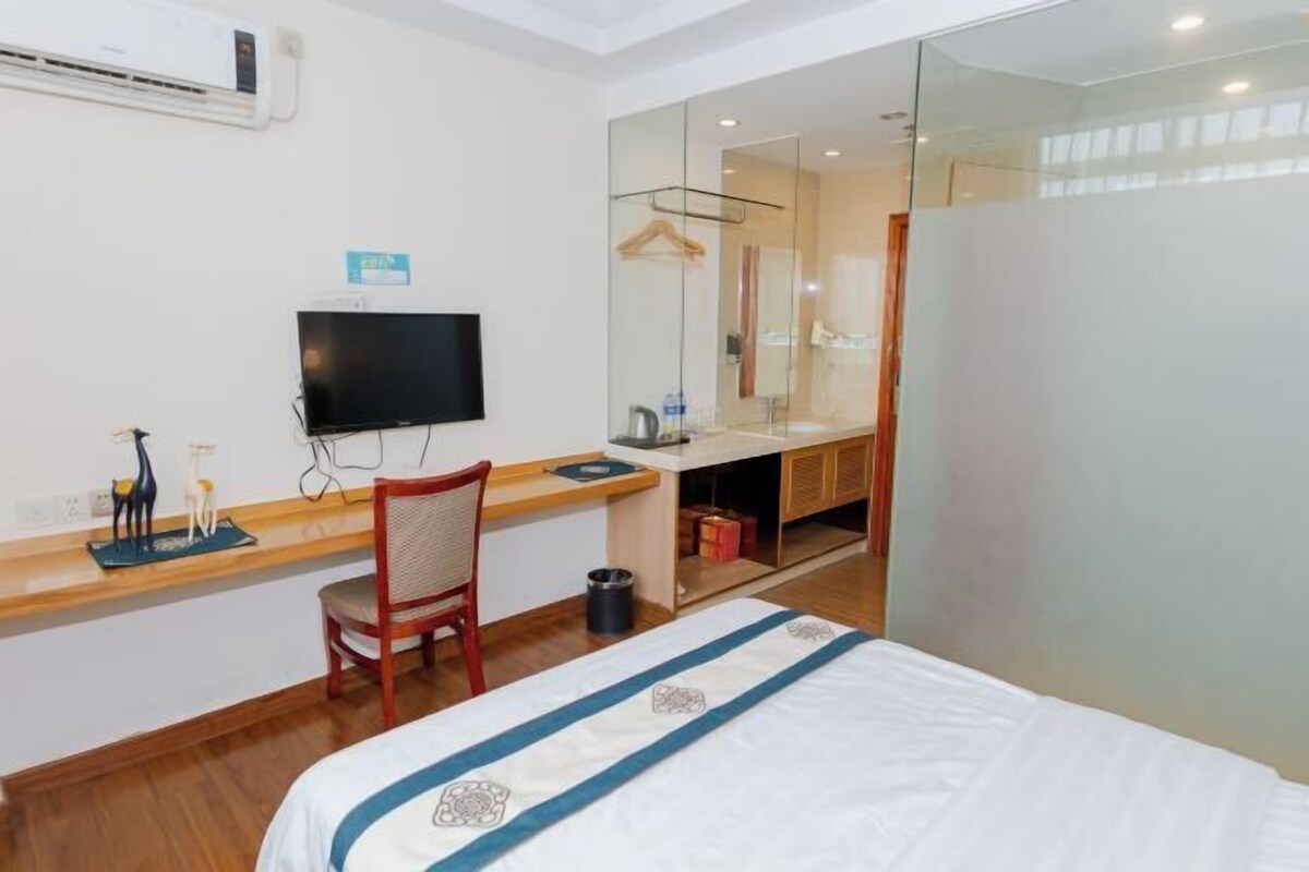 A hotel room with a bed, a desk with a chair, a TV, a mirror, and a wardrobe.