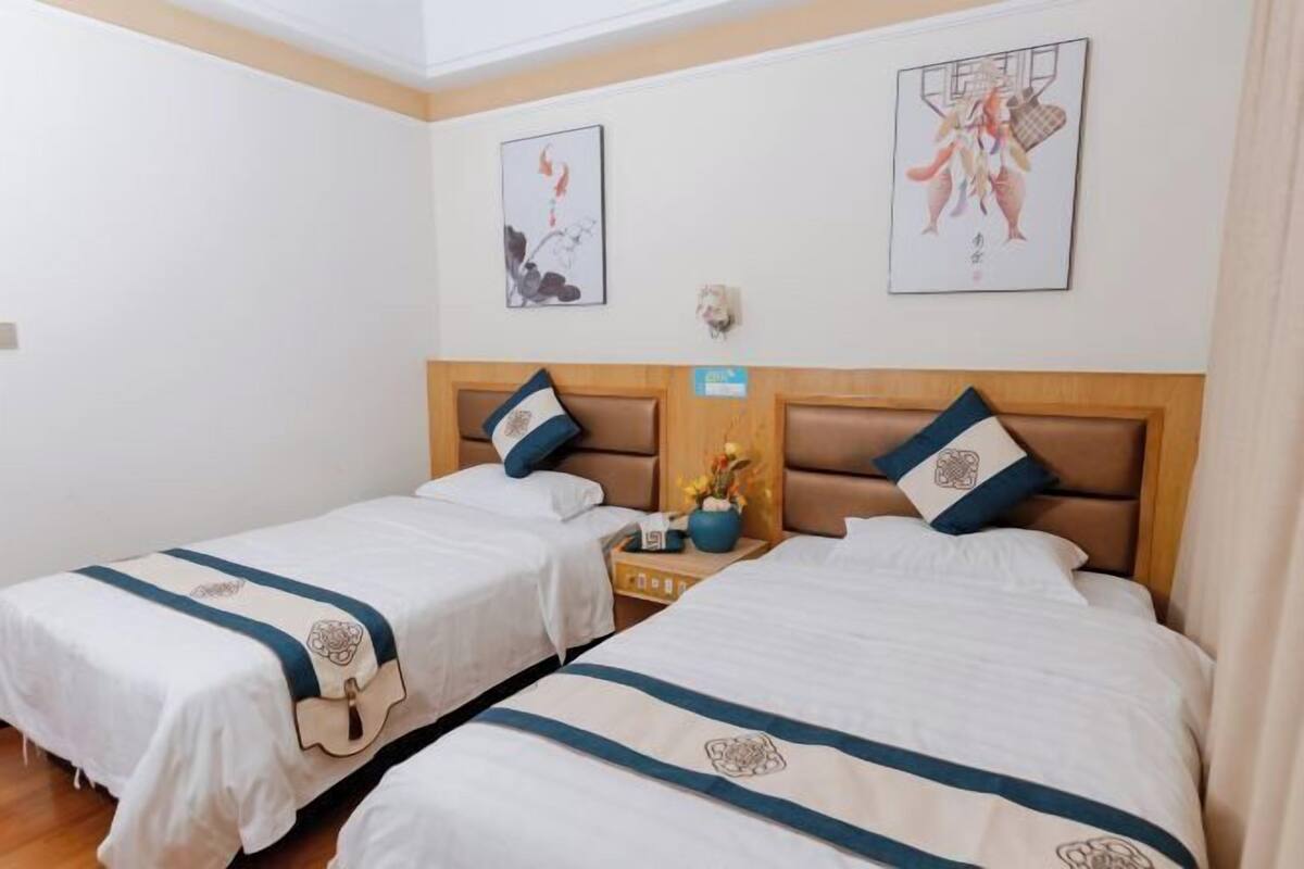 A hotel room with two beds, each with a headboard and pillow, a nightstand with a vase of flowers, and artwork on the walls.