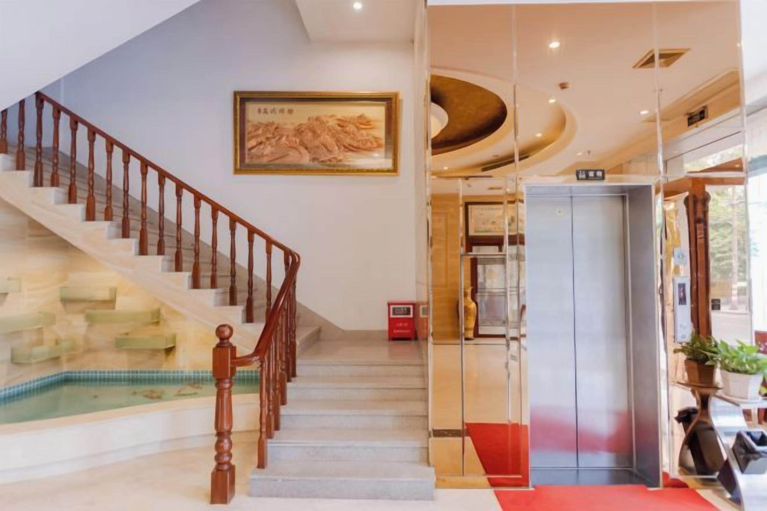 A hotel lobby with a staircase, a painting, an elevator, and a red carpet.