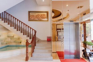 A hotel lobby with a staircase, a painting, an elevator, and a red carpet. - Meiyamei Hostel (Kaiping)