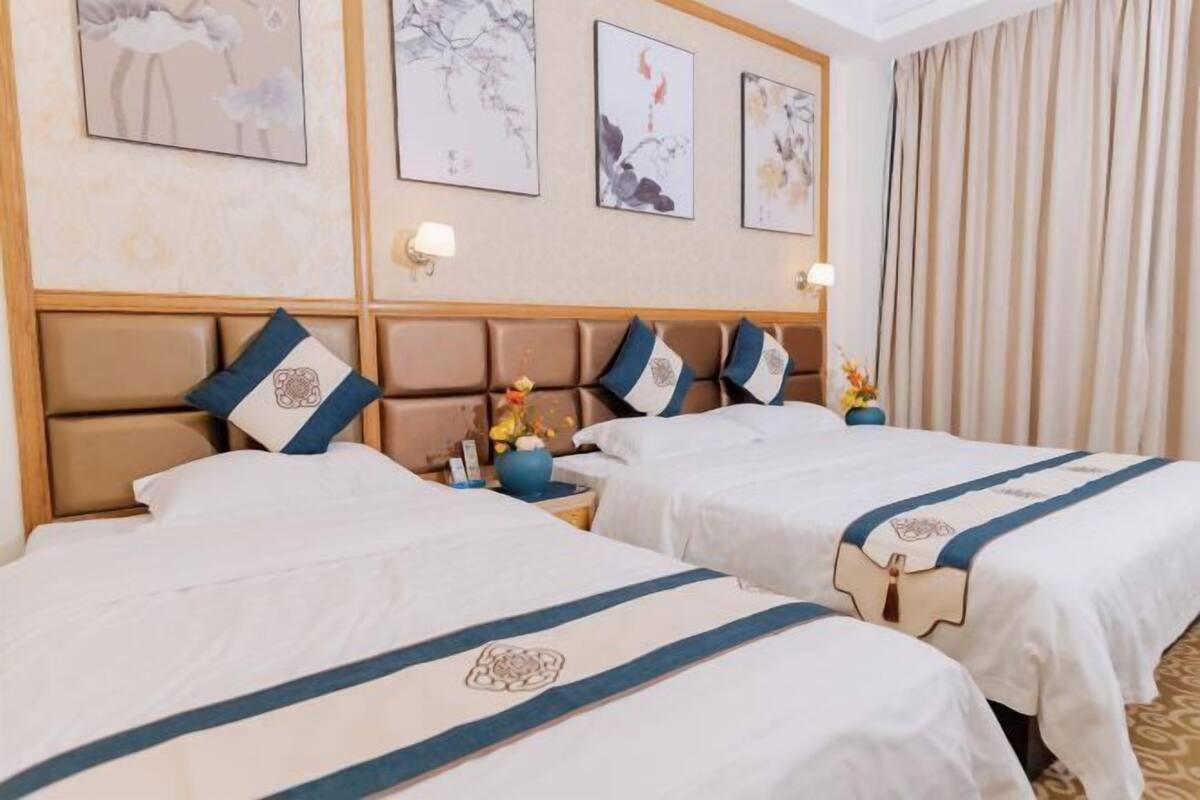 A hotel room with two beds, a wooden headboard, wall art, and a nightstand with a vase.