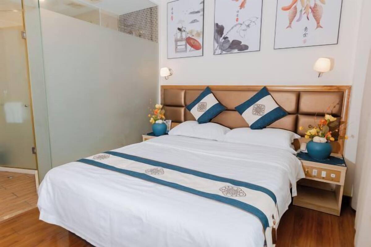 A hotel room with a bed, bedside tables, a nightstand, and artwork on the wall.