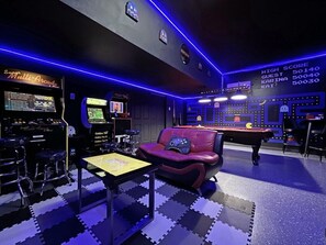 A gaming room with arcade machines, a pool table, and a red gaming chair.