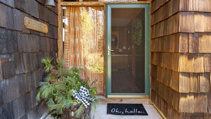 A wooden cabin entrance with a glass door, a doormat, and a small potted plant with a checkered bow. - The Connecticut Chalet - On 5 Acres! (Southington)