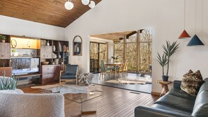 A spacious living room with a wooden ceiling, a glass coffee table, a sofa, and a dining area with a view of trees. - The Connecticut Chalet - On 5 Acres! (Southington)