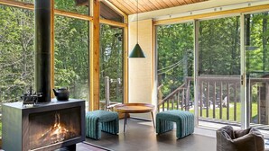 A modern interior with a wood-burning stove, large windows, and a deck area. - The Connecticut Chalet - On 5 Acres! (Southington)